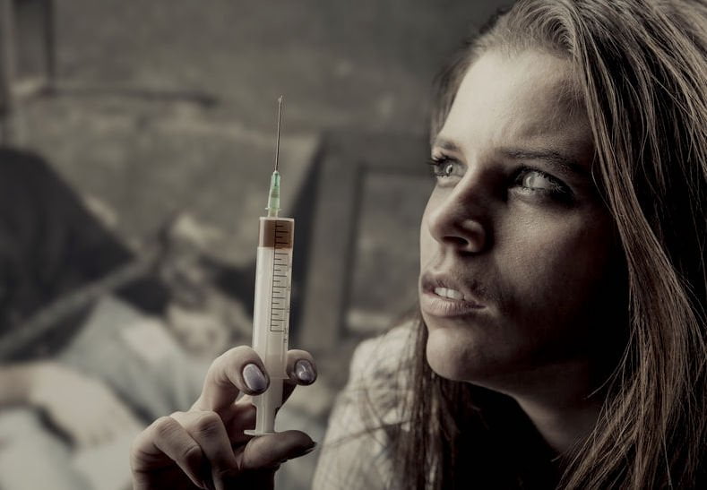 addicted traumatized woman with a needle and dark emotional face